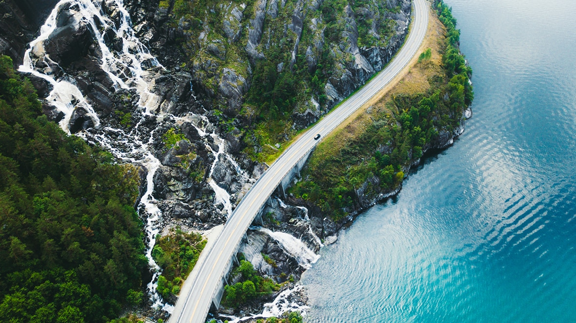Arial image of road alongside mountain and body of water.