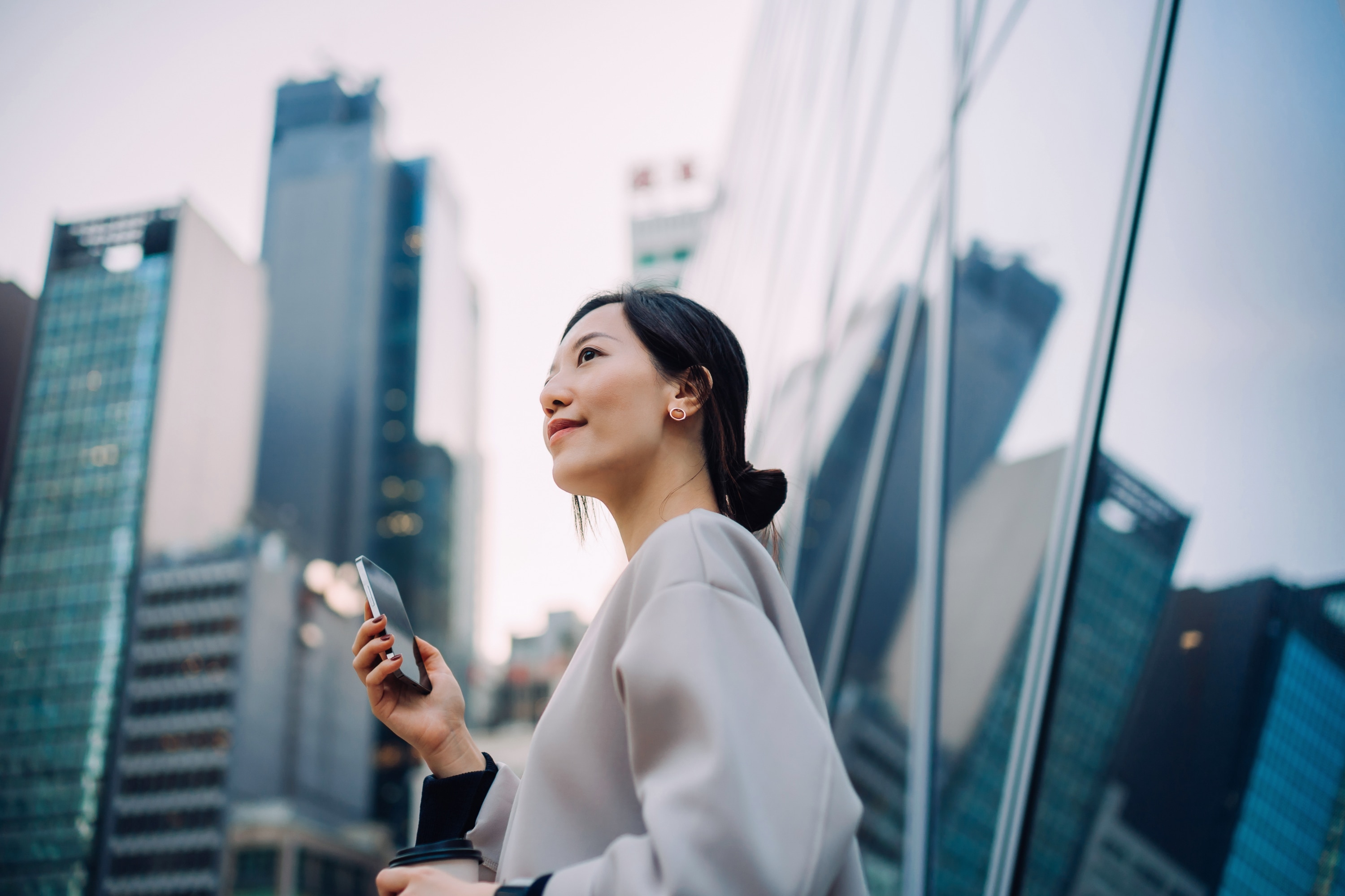 Image of woman standing in front of skyscrapers on mobile phone smiling.