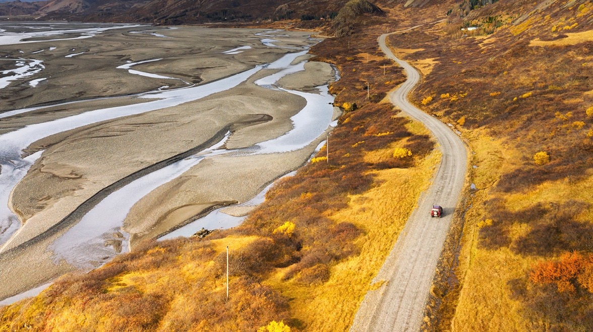 A winding road runs alongside a river through an autumn landscape with golden and orange vegetation.