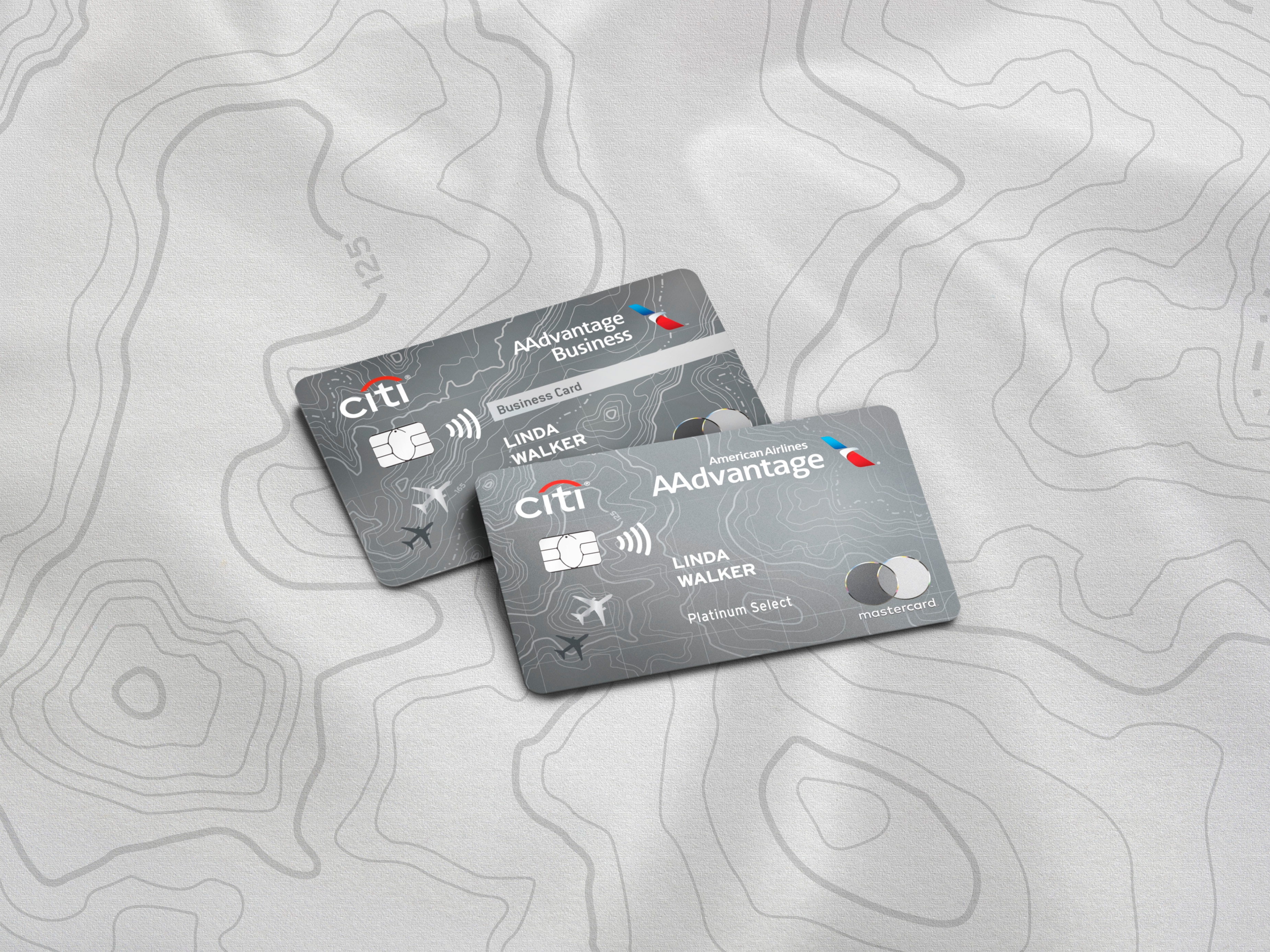 Two Citi AAdvantage credit cards, the Citi® / AAdvantage® Business Card and the American Airlines AAdvantage® Platinum Select® Mastercard®, are displayed on a stylized background with a topographical map design. The cards themselves share a modern, gray design aesthetic. Key visual elements on both include the Citi logo, the American Airlines AAdvantage logo, the cardholder name 'LINDA WALKER', an EMV chip and a contactless payment symbol. The Platinum Select card also features the Mastercard logo.